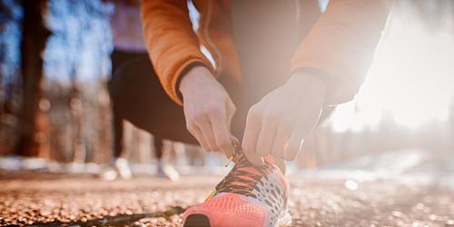 person running outdoors stopping to tie shoe laces